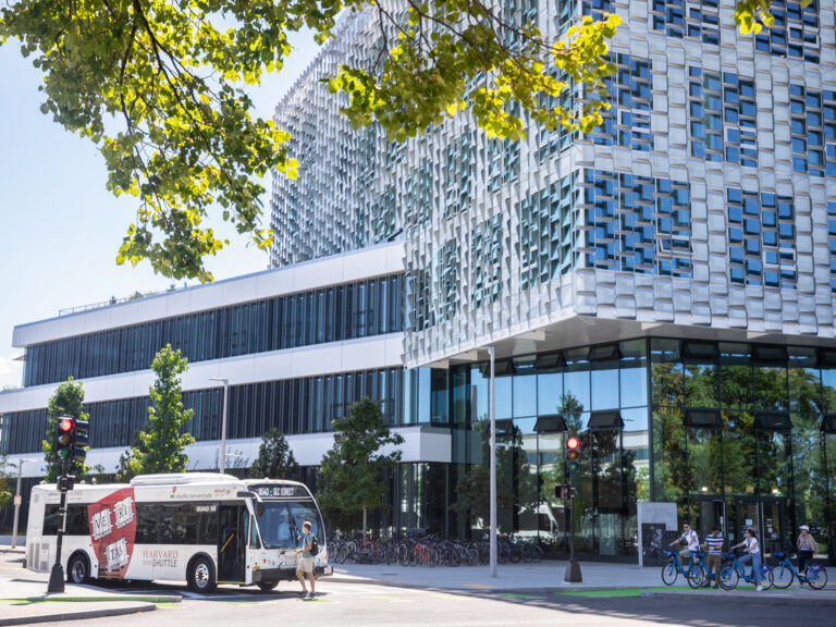 Buses from Harvard Shuttle Services pick up students at The Science and Engineering Complex (SEC) as people pass by on Bluebikes. Kris Snibbe/Harvard Staff Photographer