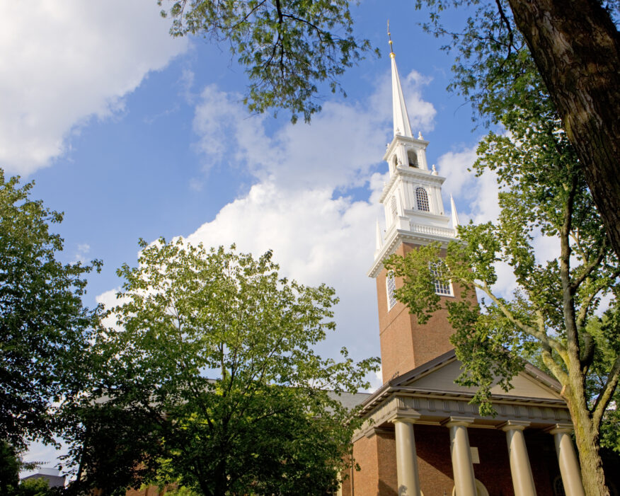 Harvard's Memorial Church against a blue sky and framed by trees.